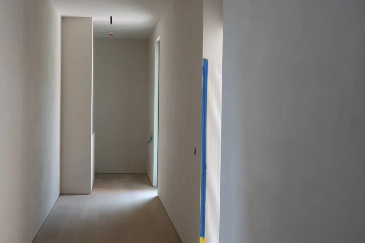 Minimalist hallway with light, smooth mineral lime walls and a natural wood floor, the kind of finish interior designers specify with Marmorino plaster in Miami