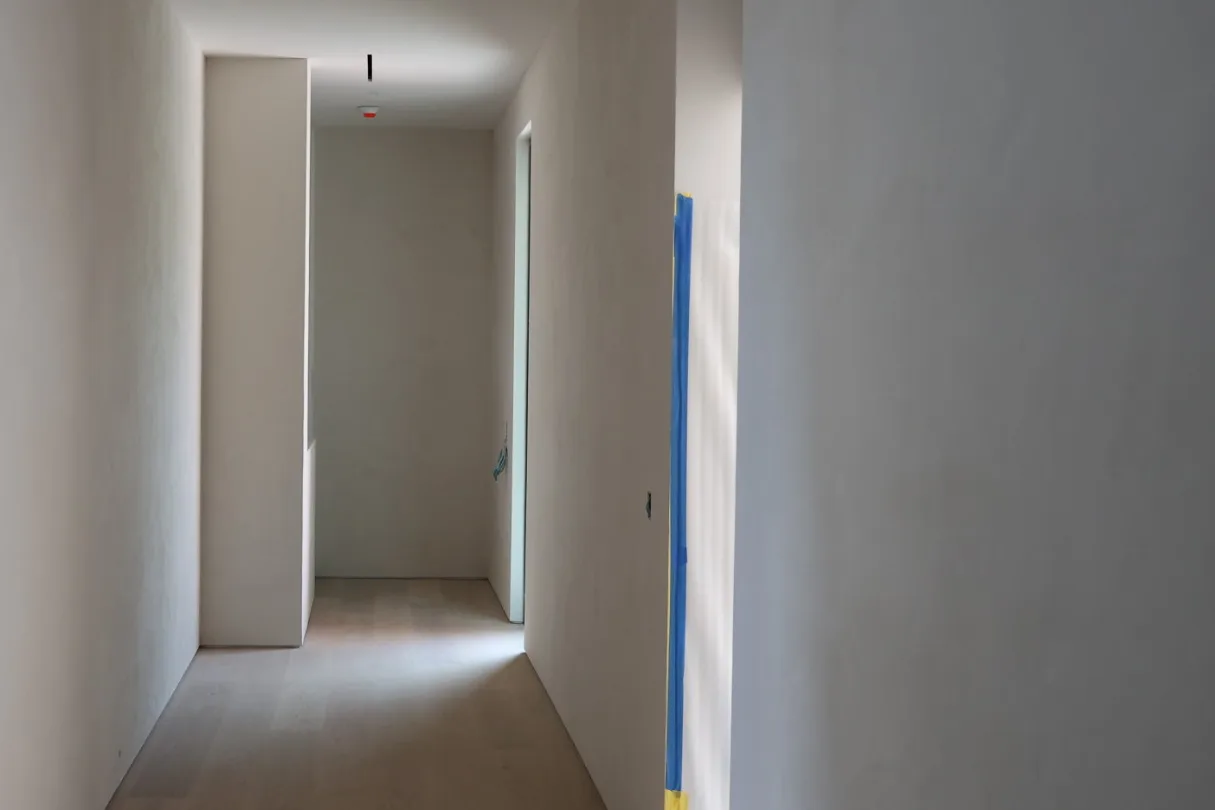 Minimalist hallway with light, smooth mineral lime walls and a natural wood floor, the kind of finish interior designers specify with Marmorino plaster in Miami